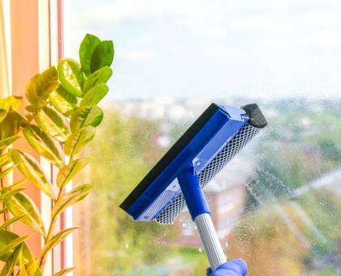 Employee hand in rubber protective glove cleans window with foam and puller. General spring cleaning